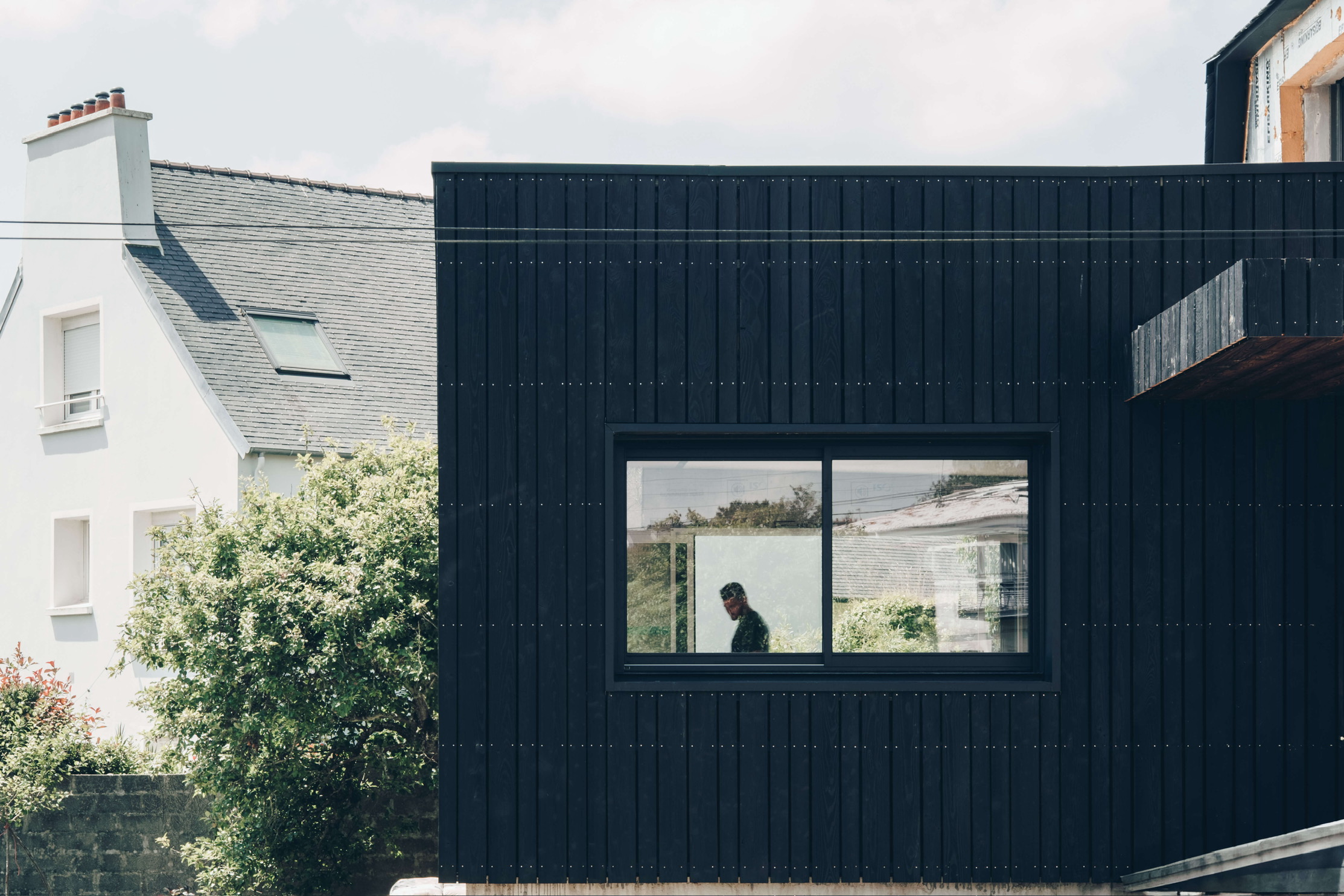 Photo d'une extension en bardage bois brûlé noir et une fenêtre laissant voir une silhouette à l’intérieur.